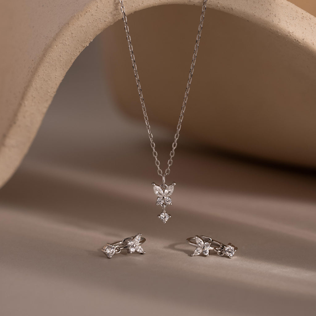 The Diamond Butterfly Drop Jewelry Set includes a silver butterfly drop necklace and matching huggie earrings, elegantly displayed on a neutral backdrop.
