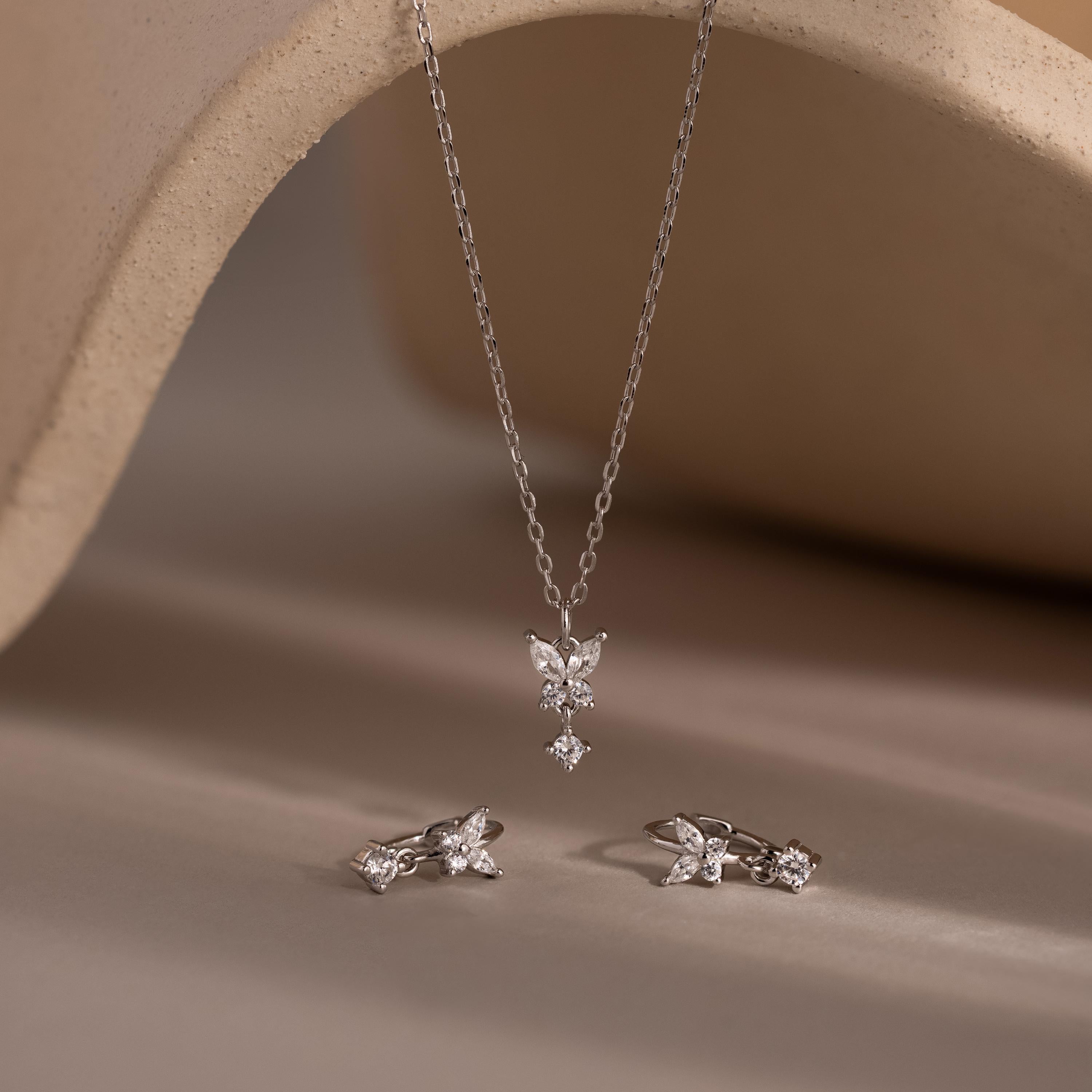The Diamond Butterfly Drop Jewelry Set includes a silver butterfly drop necklace and matching huggie earrings, elegantly displayed on a neutral backdrop.