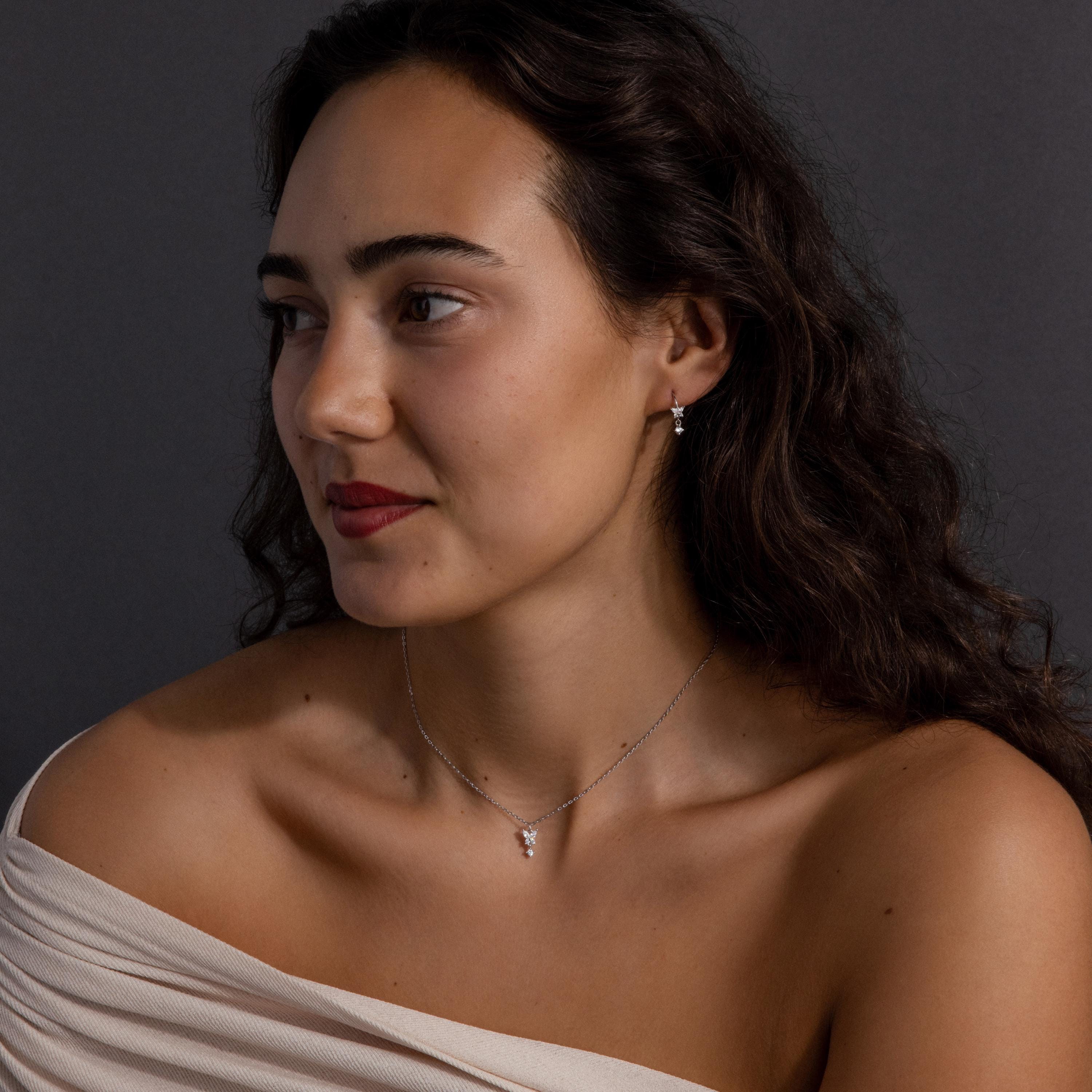 A woman with wavy dark hair poses in an off-shoulder top, wearing the Diamond Butterfly Drop Jewelry Set in Sterling Silver, against a dark background.