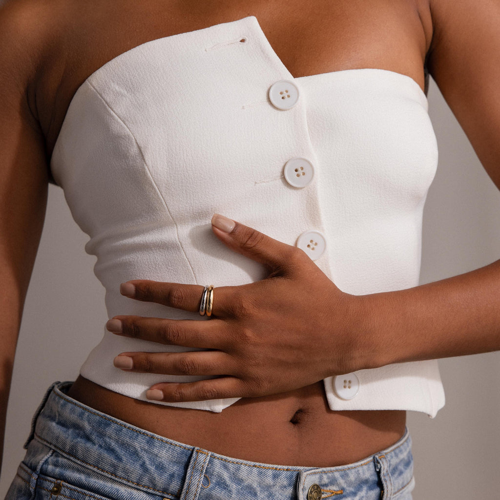 A person in a white asymmetrical buttoned top and jeans, hand on waist, captures a modern classic look highlighted by the Mixed Metal Dome Ring Set—versatile jewelry perfect for any occasion.