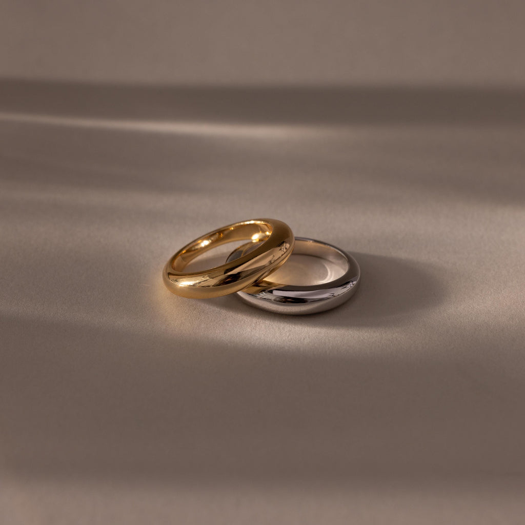 The Mixed Metal Dome Ring Set—featuring a gold and a silver ring side by side on a smooth surface with soft lighting—captures modern style and versatility, making it the perfect jewelry choice for any occasion.