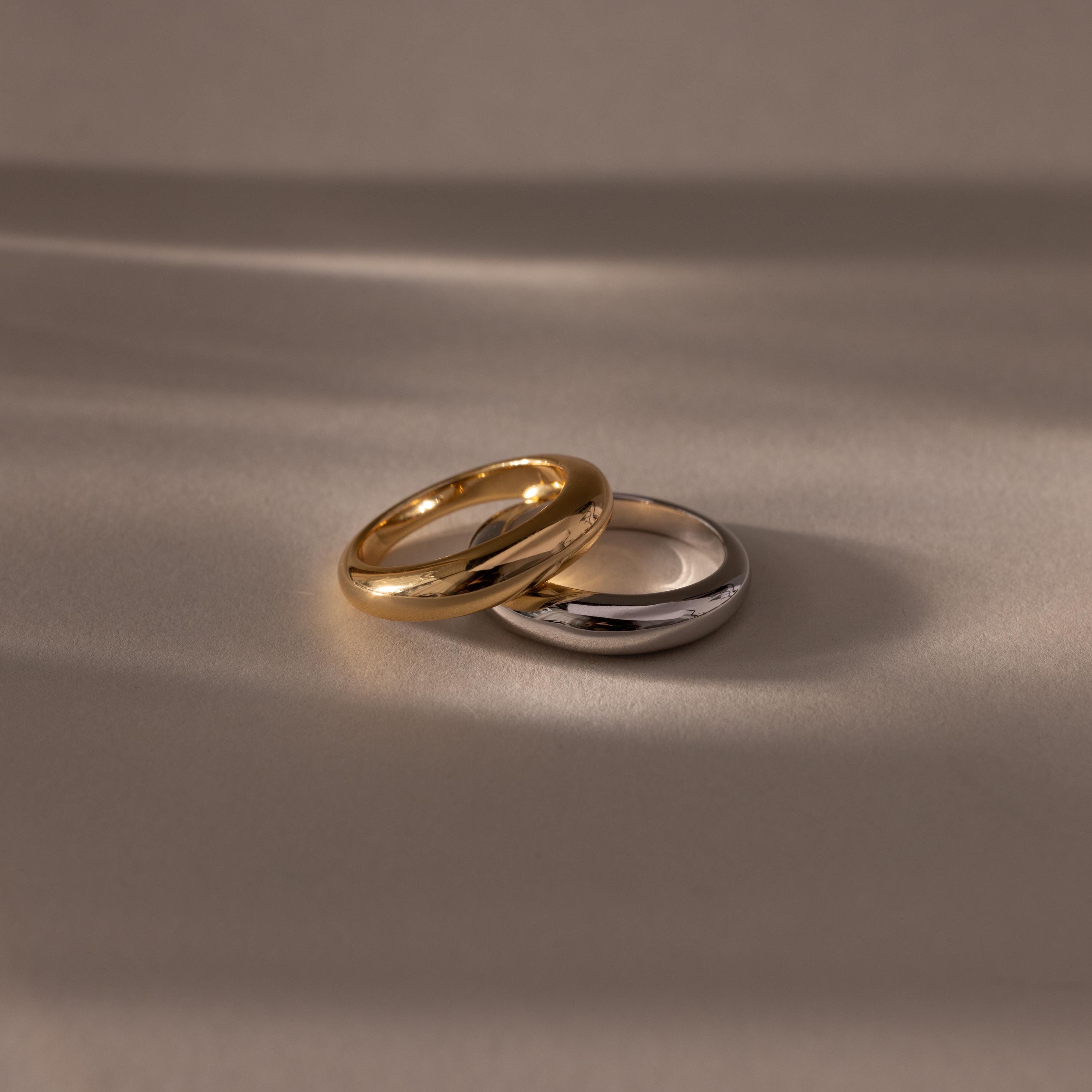 The Mixed Metal Dome Ring Set—featuring a gold and a silver ring side by side on a smooth surface with soft lighting—captures modern style and versatility, making it the perfect jewelry choice for any occasion.