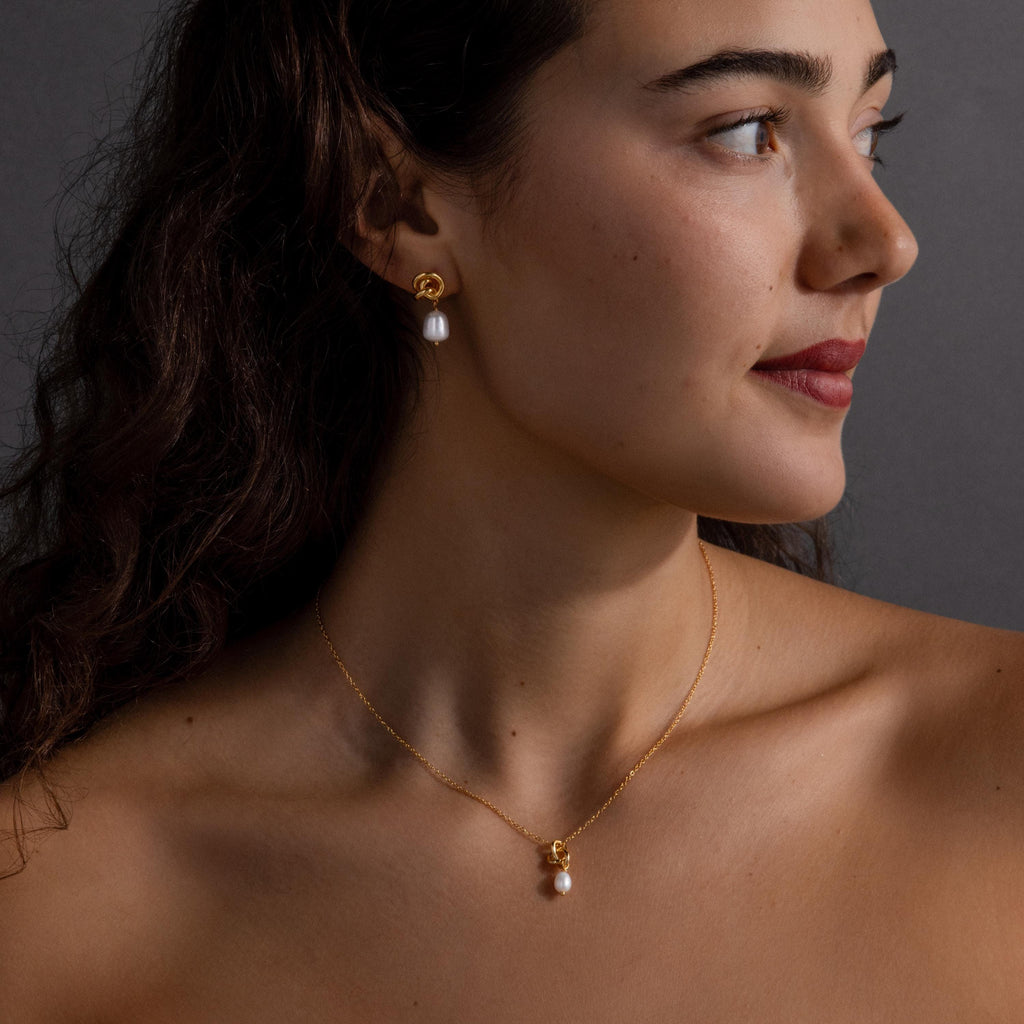 Woman with wavy hair wears the Pearl Knot Necklace & Earrings Set, looking to the right—a stunning gift for a wife who appreciates timeless elegance.