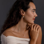 Woman in off-shoulder top wearing the Pearl Knot Necklace & Earrings Set, featuring gold and pearl accents, poses against a dark background—an elegant look, perfect as a gift for your wife.