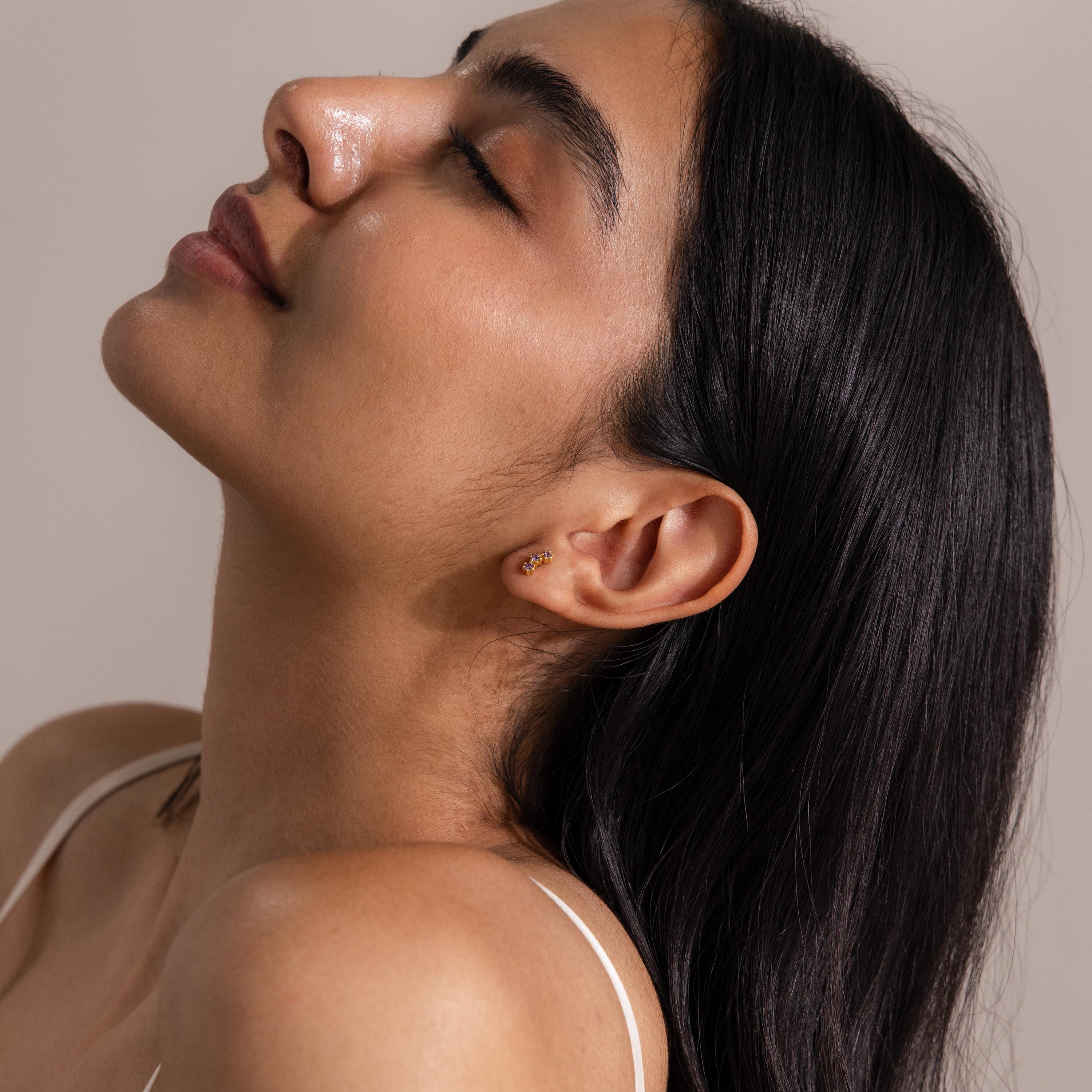 A woman with long dark hair tilts her head back, eyes closed, highlighting Birthstone Cluster Flatback Studs in her curated earring stack.