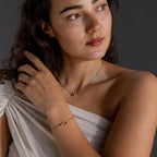 A woman models the Interlocking Circles Necklace and Bracelet Set, featuring a minimalist gold design with an off-shoulder top, while gazing thoughtfully to the side.