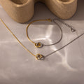 The Interlocking Circles Necklace and Bracelet Set, featuring gold and silver circles, rests on a neutral surface with soft shadows, highlighting this minimalist jewelry set.