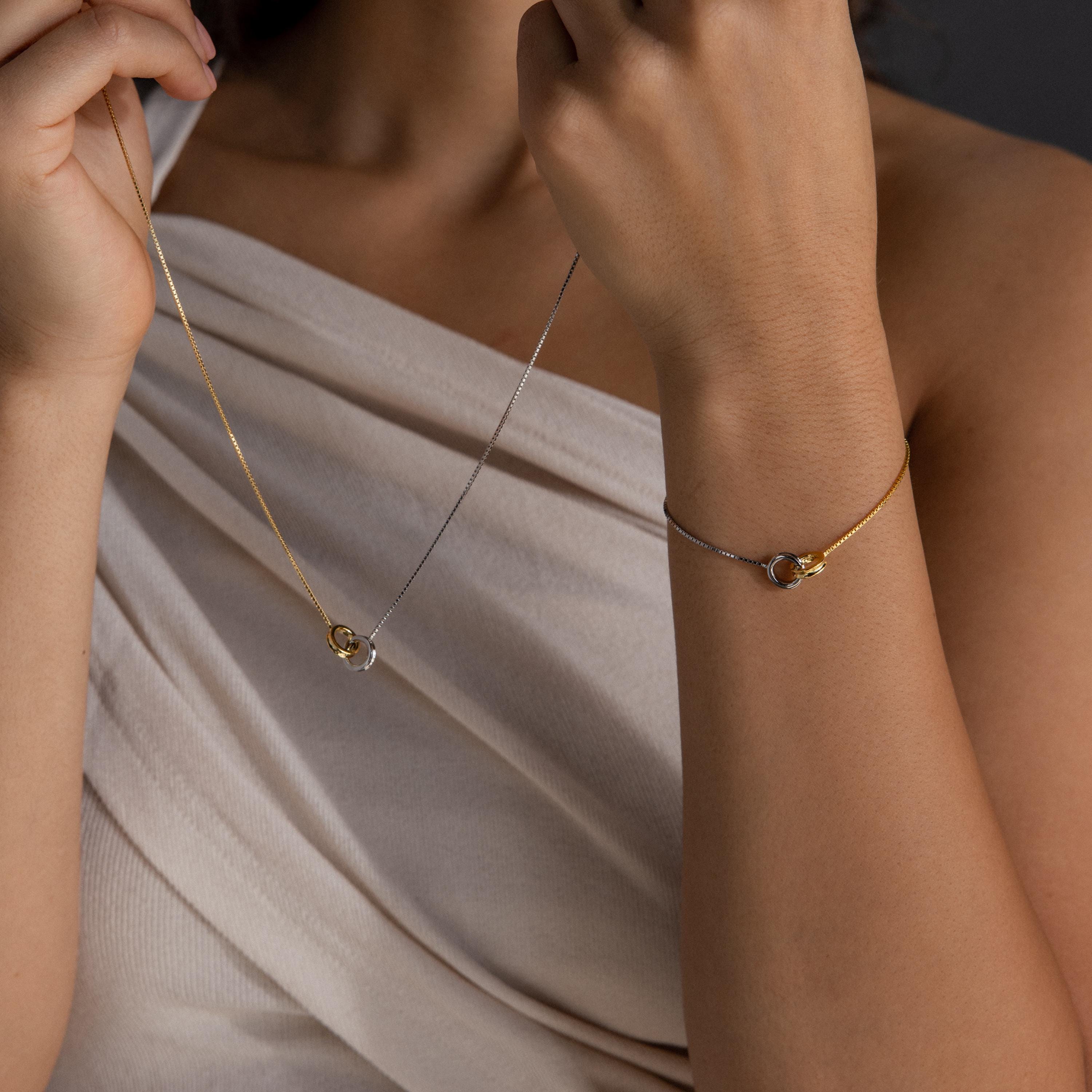 A woman in a cream top showcases the Interlocking Circles Necklace and Bracelet Set—a chic minimalist jewelry set with mixed metals and interlocking rings, perfect for any occasion.