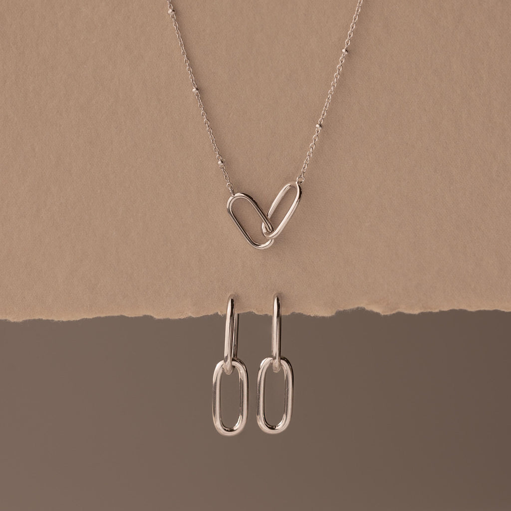 Linked Charm Necklace and Earrings Set in Sterling Silver, featuring interlocking hearts and oval links, shown on a beige background—an ideal anniversary gift.