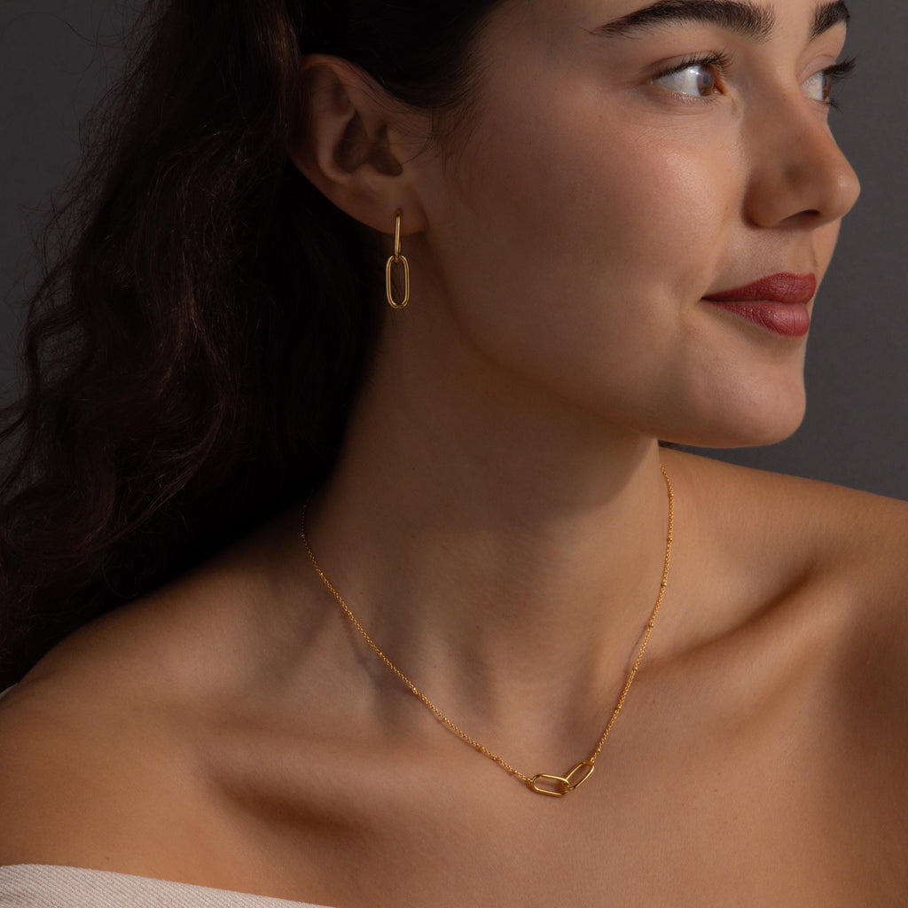 Woman with dark hair smiles slightly while wearing the Linked Charm Necklace and Earrings Set—an elegant choice for an anniversary gift.