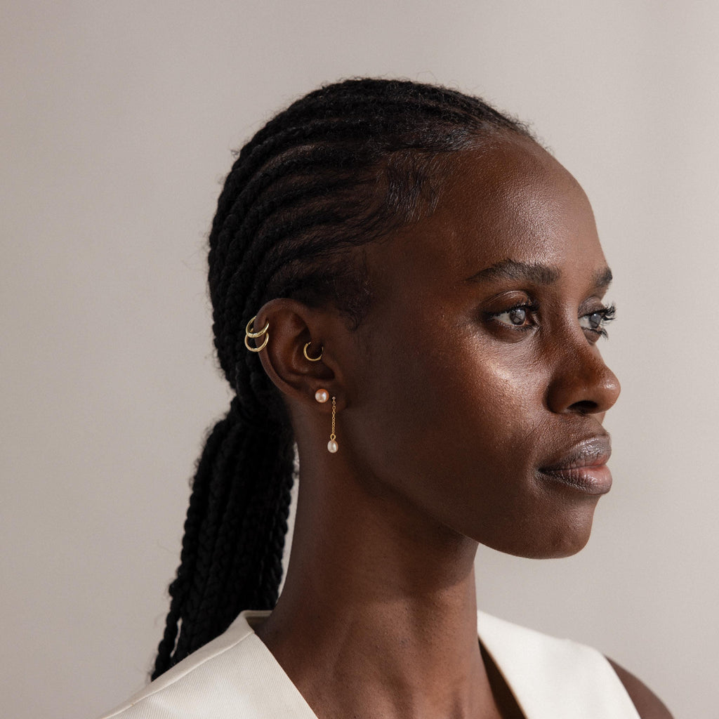 A woman with braided hair wears gold hoops and the Pink Pearl Studs, gazing to the side against a blush-toned background.