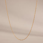 The Dainty Paperclip Necklace features small rectangular gold links, ideal for layering as a simple, elegant accessory, shown against a plain beige background.