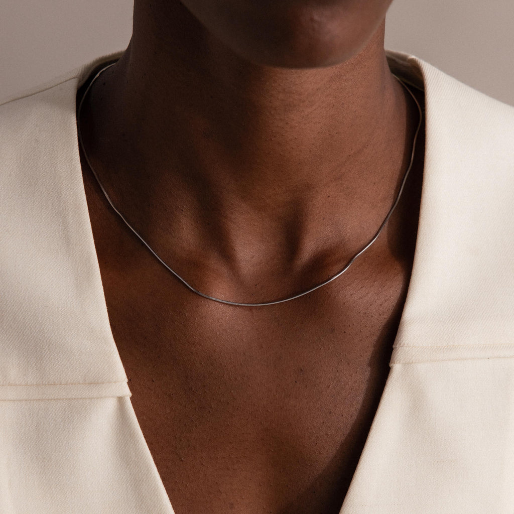 Wearing the Dainty Herringbone Necklace in Sterling Silver with an off-white blazer, a person—shown from shoulders to chin—creates a sleek, layered look.