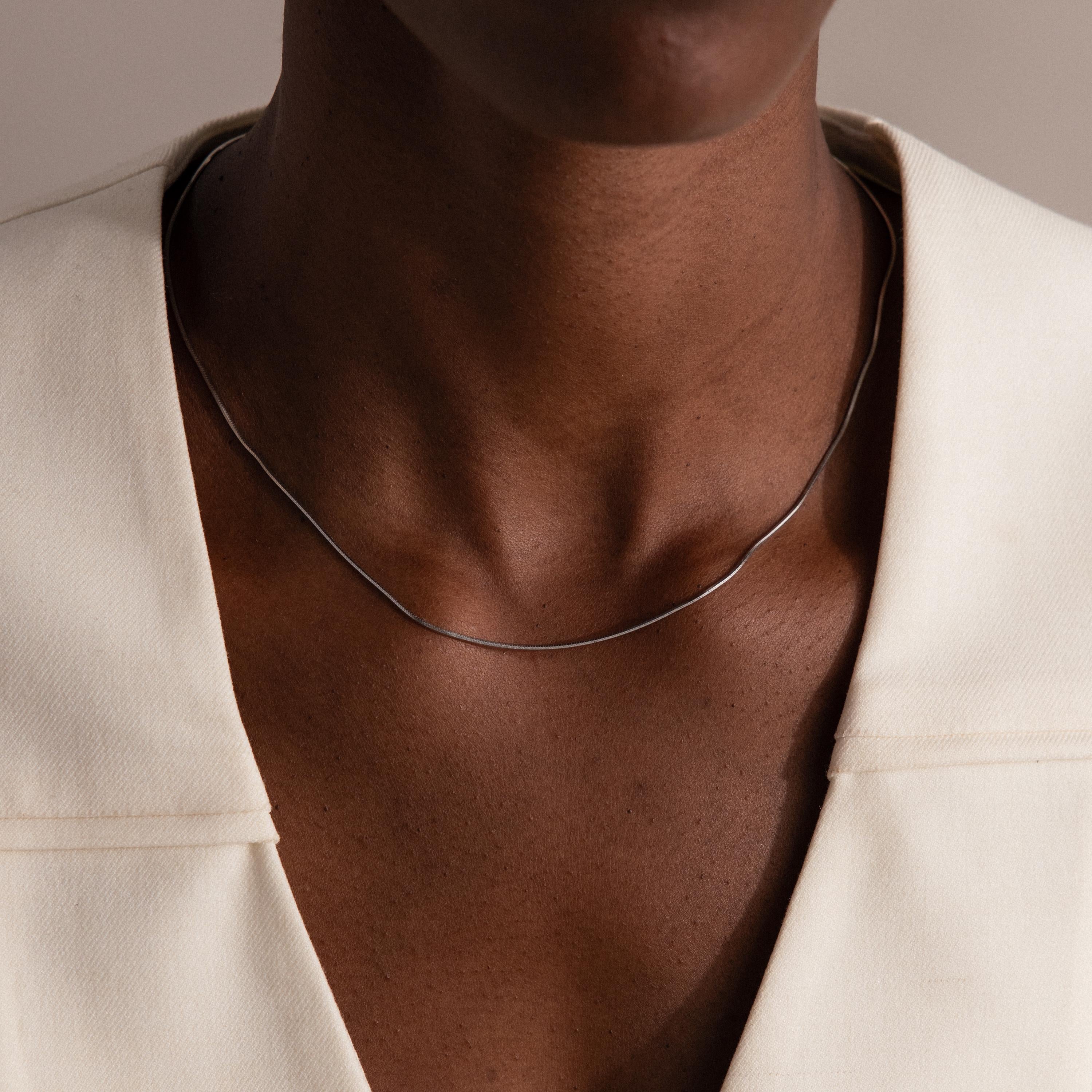 Wearing the Dainty Herringbone Necklace in Sterling Silver with an off-white blazer, a person—shown from shoulders to chin—creates a sleek, layered look.