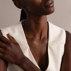 Woman wearing a sleeveless white top and the Dainty Herringbone Necklace in 18K Gold, her hand resting on her shoulder.