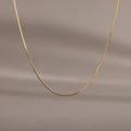 The Dainty Herringbone Necklace features a delicate curve, beautifully displayed against a simple beige background.