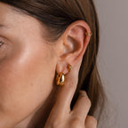 Close-up of a person's ear with three Bold Teardrop Earrings and a gold ear cuff, showcasing modern jewelry style with hair tucked behind the ear.