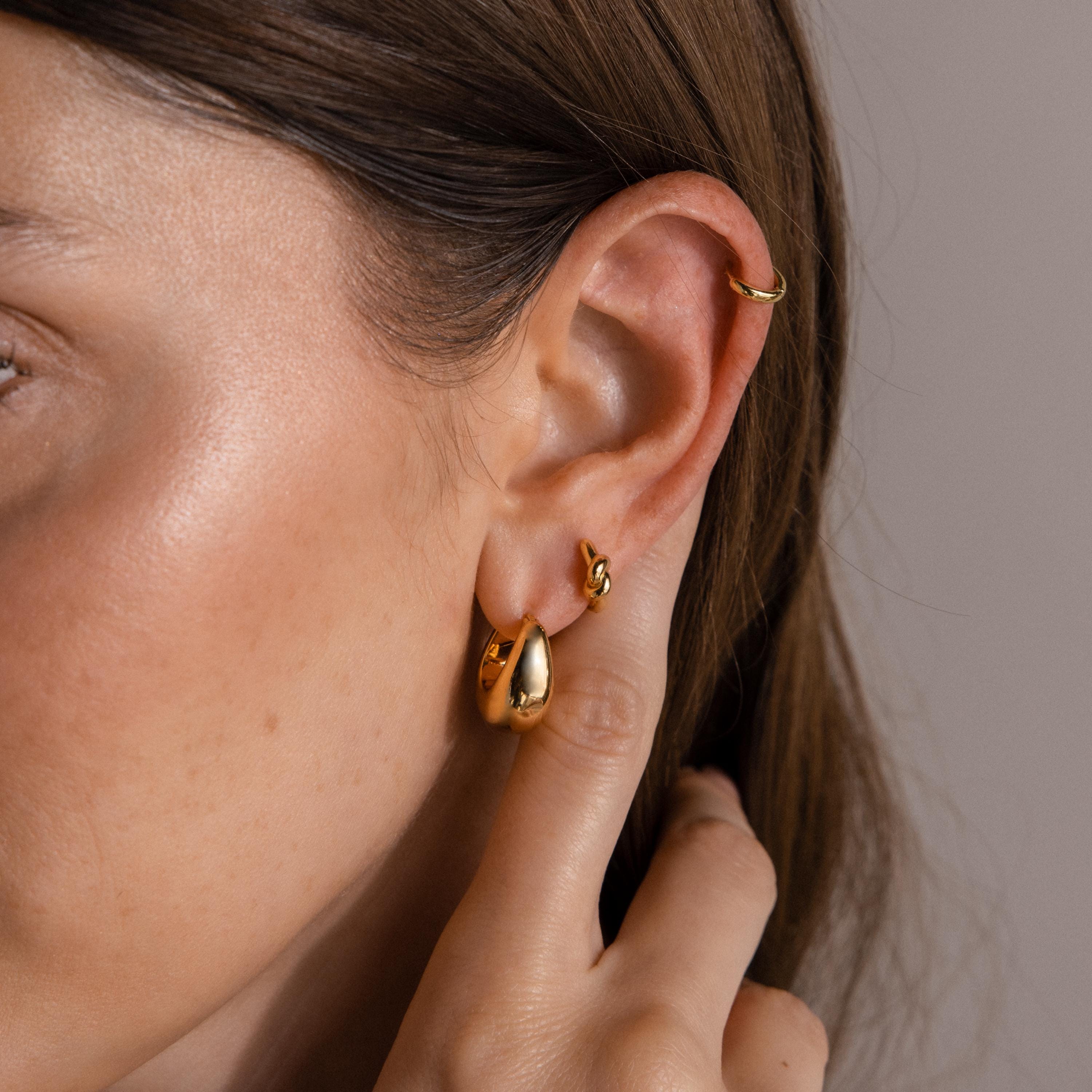 Close-up of a person's ear with three Bold Teardrop Earrings and a gold ear cuff, showcasing modern jewelry style with hair tucked behind the ear.