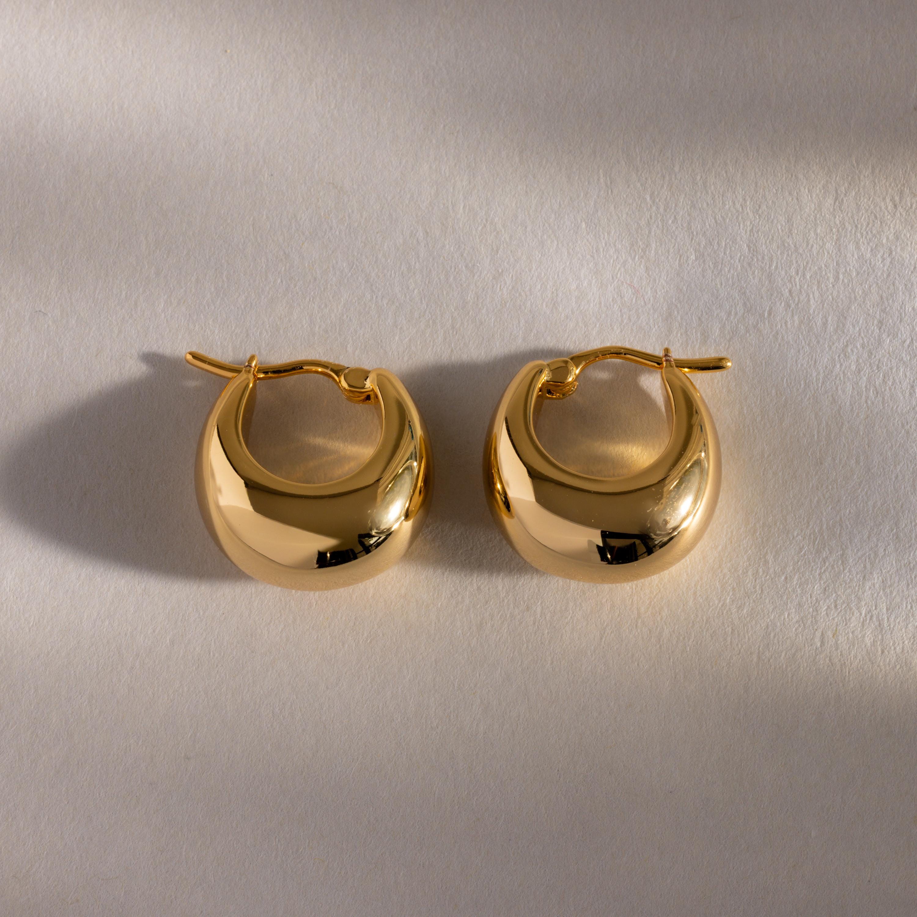 Bold Teardrop Earrings in 18K Gold with a chunky, rounded design and high polish finish displayed on a light textured surface with soft shadows.