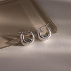 The Bold Teardrop Earrings, with their shiny silver finish, rest on a light, reflective surface—ideal for anyone who loves modern jewelry.