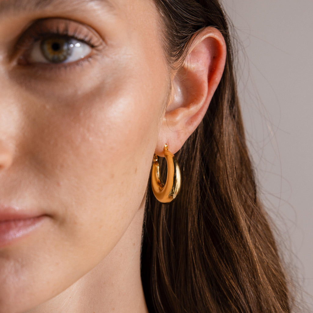 Close-up of a woman’s face with brown hair tucked behind her ear, showcasing the Sculpted Hoops—modern classic earrings featuring a high shine finish.