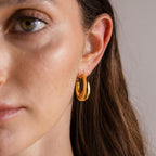 Close-up of a woman’s face with brown hair tucked behind her ear, showcasing the Sculpted Hoops—modern classic earrings featuring a high shine finish.