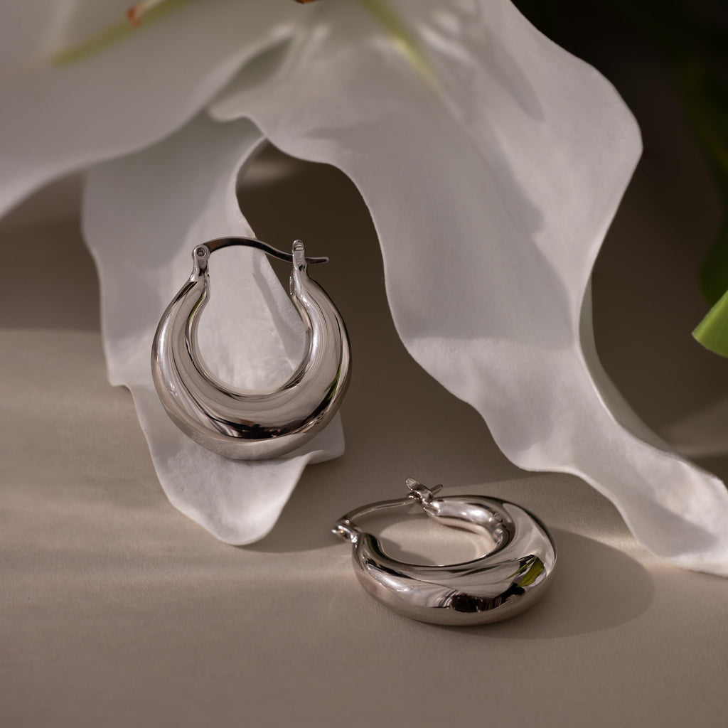 Sculpted Hoops with a high-shine finish are displayed on white flower petals under soft lighting.