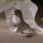 Sculpted Hoops with a high-shine finish are displayed on white flower petals under soft lighting.