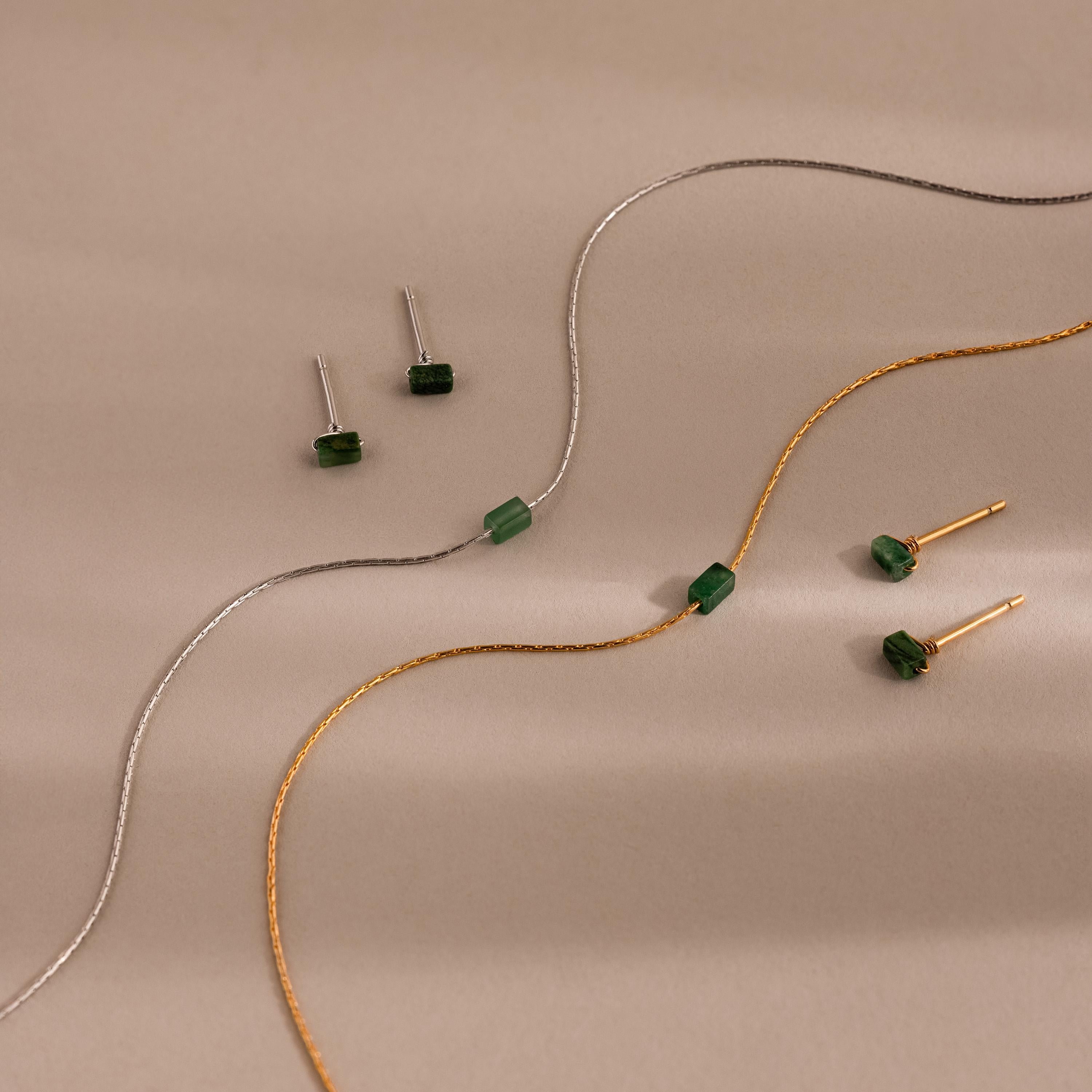 The Jade Bar Jewelry Set, featuring two pairs of jade stud earrings and two matching bar necklaces, is elegantly displayed on a beige background.