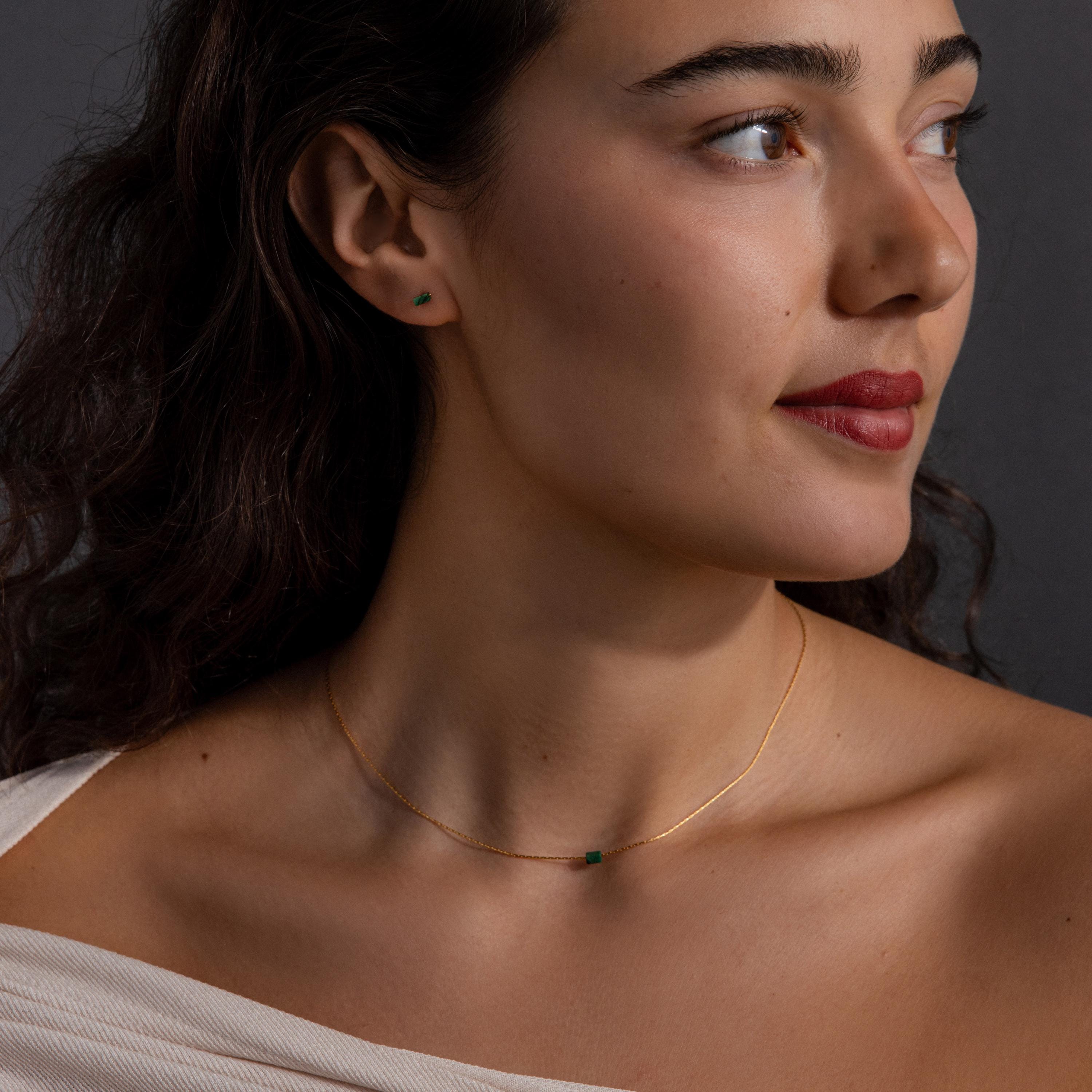 Woman with wavy brown hair wearing the Jade Bar Jewelry Set, featuring a gold jade bar necklace and matching green jade stud earrings, looking to the side.