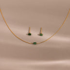 The Jade Bar Jewelry Set features a gold necklace and earrings with petite green jade stones, displayed on a beige background—an elegant accessory to enhance any outfit.