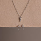 Diamond Butterfly Drop Jewelry Set in Sterling Silver, featuring a necklace and matching huggie earrings with butterfly-shaped pendants, displayed on textured beige paper.
