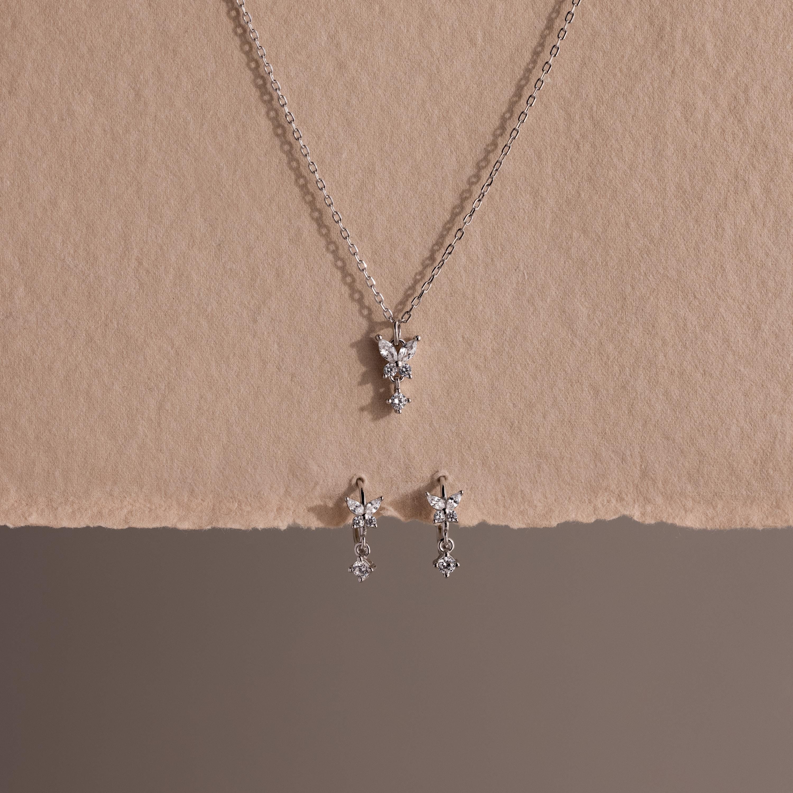 Diamond Butterfly Drop Jewelry Set in Sterling Silver, featuring a necklace and matching huggie earrings with butterfly-shaped pendants, displayed on textured beige paper.