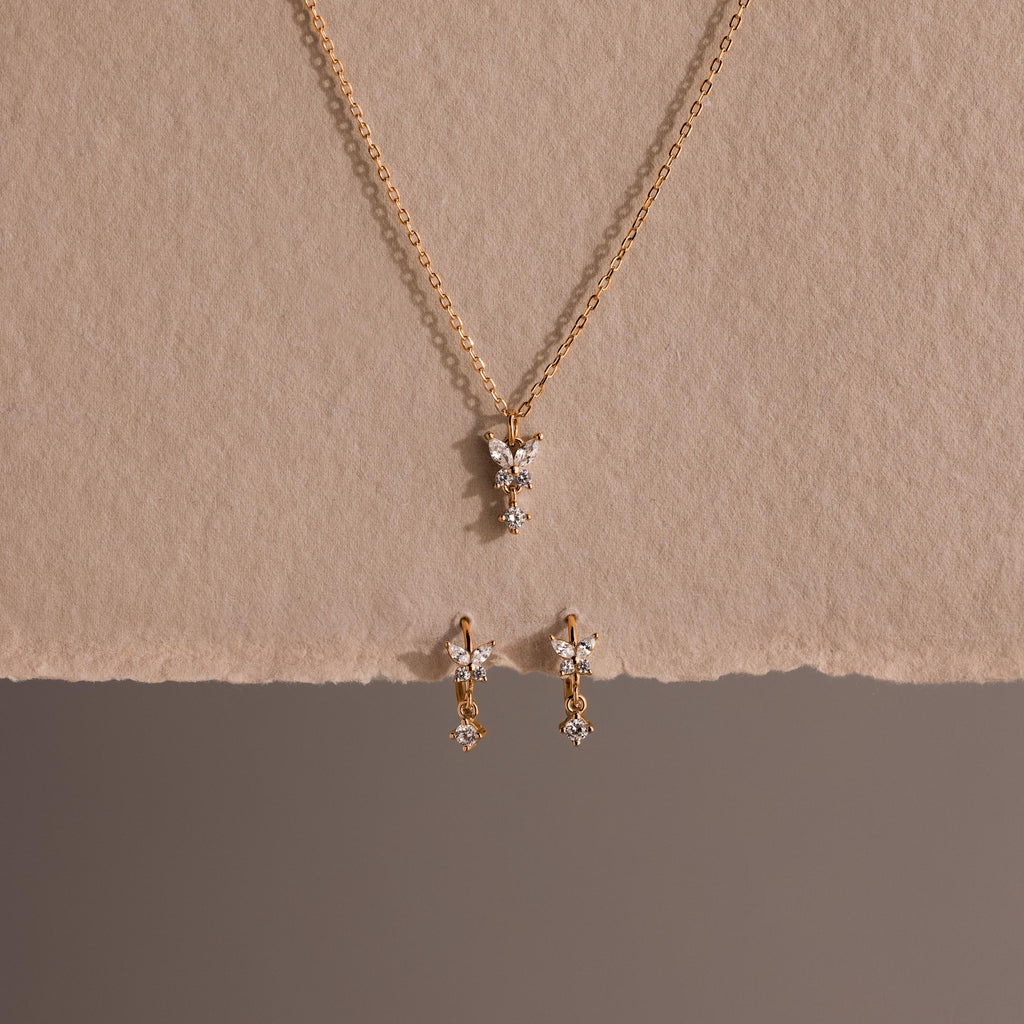 The Diamond Butterfly Drop Jewelry Set features a gold butterfly necklace and matching huggie earrings with diamond-accented pendants, displayed on a neutral textured background—perfect for fans of butterfly-inspired jewelry.