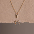 The Diamond Butterfly Drop Jewelry Set features a gold butterfly necklace and matching huggie earrings with diamond-accented pendants, displayed on a neutral textured background—perfect for fans of butterfly-inspired jewelry.