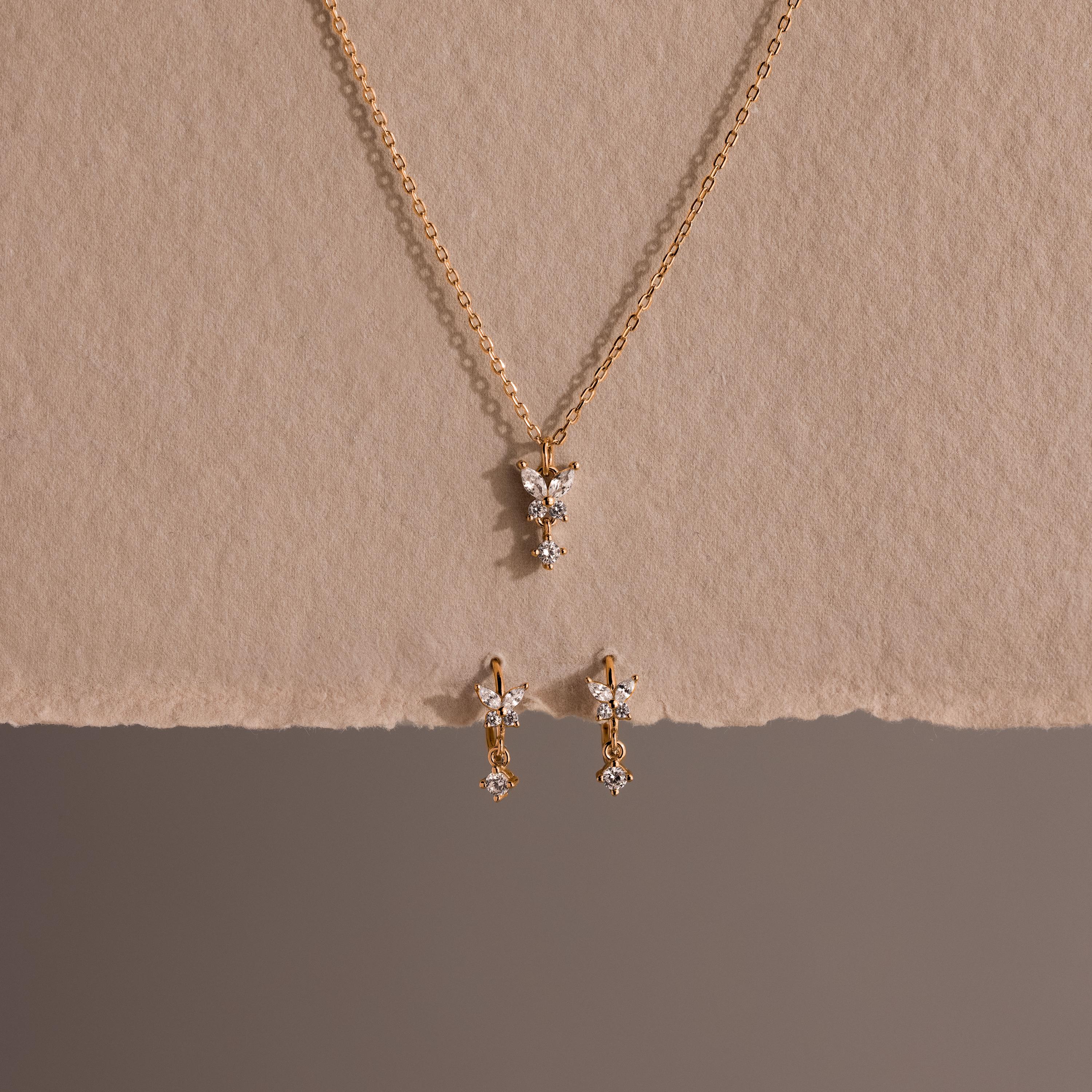 The Diamond Butterfly Drop Jewelry Set features a gold butterfly necklace and matching huggie earrings with diamond-accented pendants, displayed on a neutral textured background—perfect for fans of butterfly-inspired jewelry.