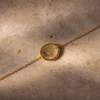 Dainty Organic Fingerprint Bracelet in 18K Gold with a round pendant featuring your unique design, displayed on a stone surface—a beautiful personalized memorial gift.