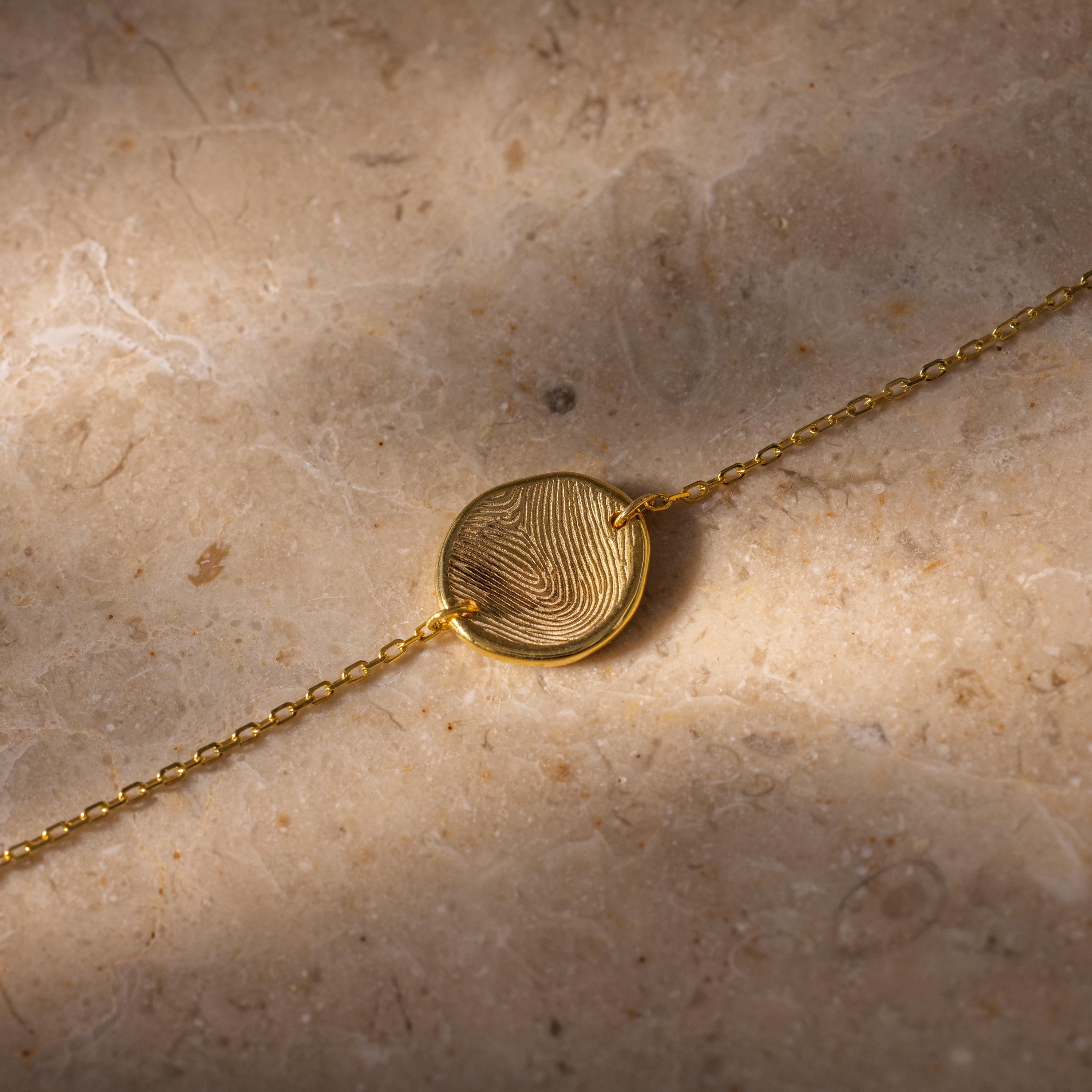 Dainty Organic Fingerprint Bracelet in 18K Gold with a round pendant featuring your unique design, displayed on a stone surface—a beautiful personalized memorial gift.
