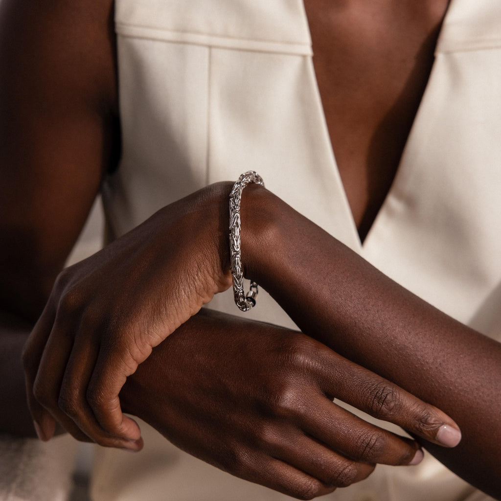 A person wearing a Byzantine Link Bracelet in White Gold rests their hands on their arm, dressed in a cream sleeveless top.