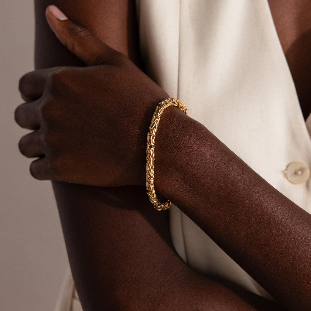 A person with crossed arms in a cream sleeveless top highlights the Byzantine Link Bracelet, making it a striking statement accessory.