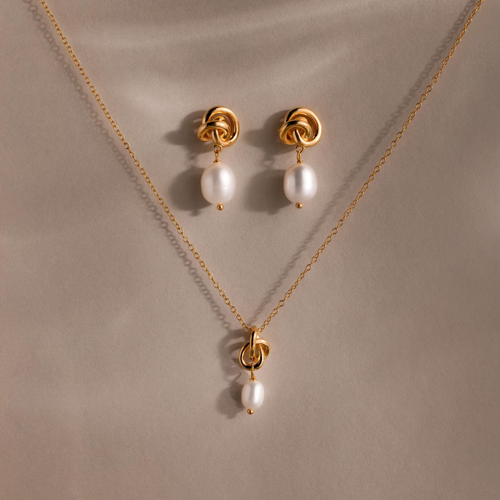 Pearl Knot Necklace & Earrings Set, featuring a gold knot design with single white pearls. Elegantly displayed on beige fabric. A thoughtful gift for your wife or someone special.