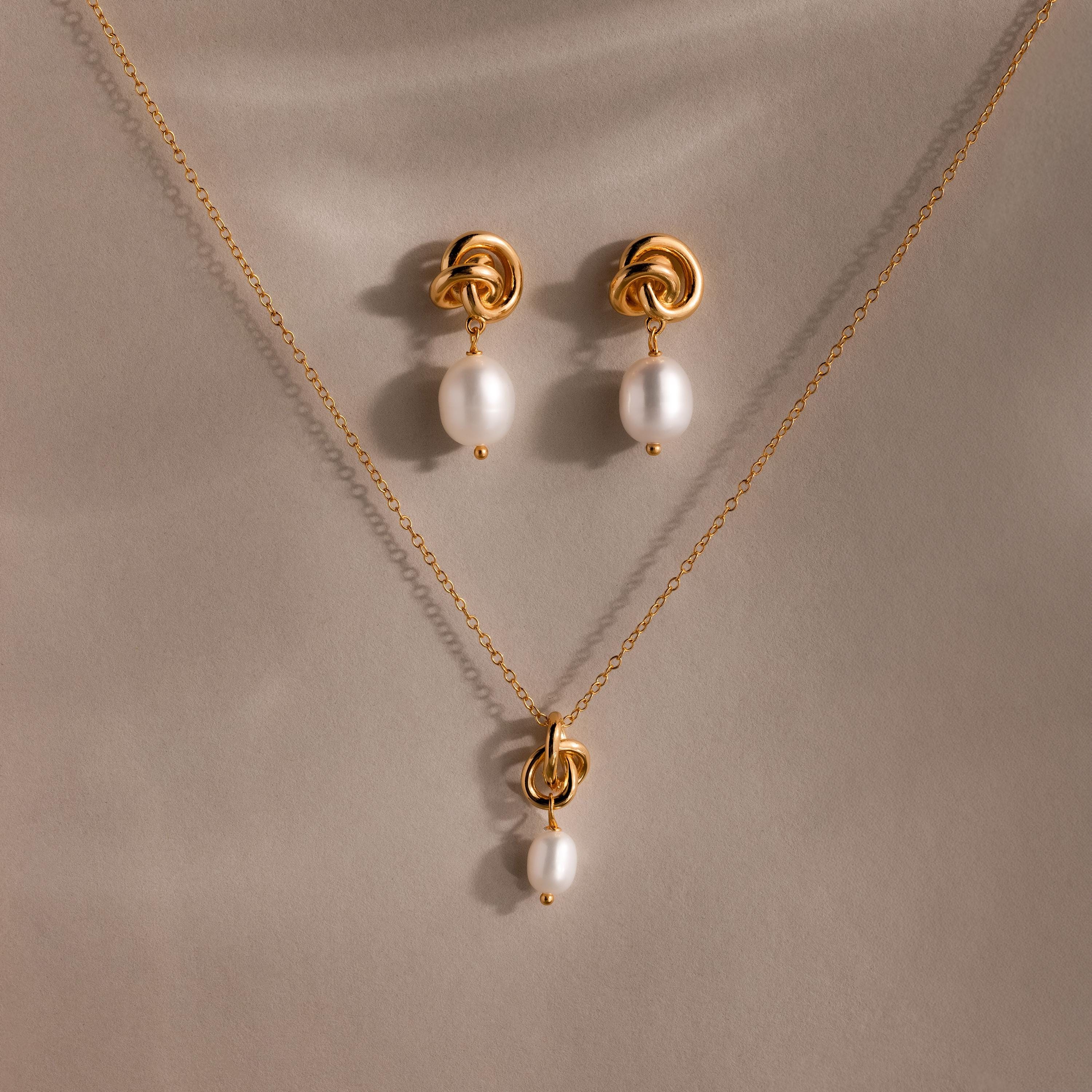 Pearl Knot Necklace & Earrings Set, featuring a gold knot design with single white pearls. Elegantly displayed on beige fabric. A thoughtful gift for your wife or someone special.