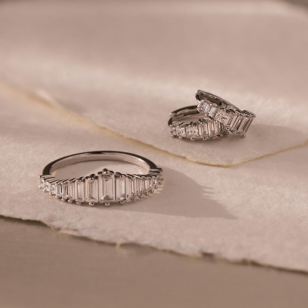 The Art Deco Diamond Earrings & Ring Set in Sterling Silver, featuring rectangular clear stones, is displayed on soft, beige textured fabric.
