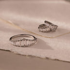The Art Deco Diamond Earrings & Ring Set in Sterling Silver, featuring rectangular clear stones, is displayed on soft, beige textured fabric.
