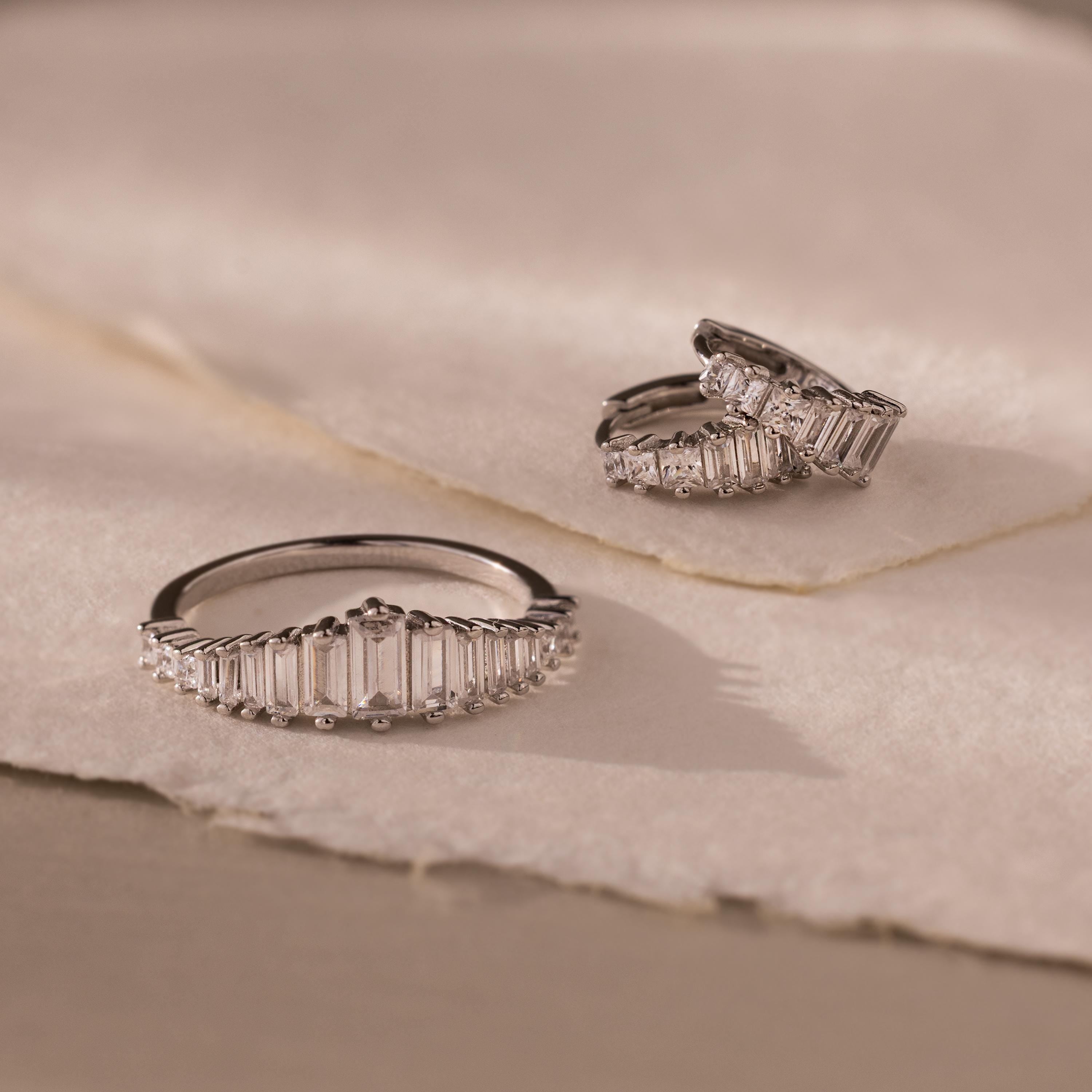 The Art Deco Diamond Earrings & Ring Set in Sterling Silver, featuring rectangular clear stones, is displayed on soft, beige textured fabric.