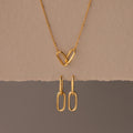 The Linked Charm Necklace and Earrings Set features two interlocking heart-shaped links and matching gold earrings, making an elegant anniversary gift displayed on a beige background.