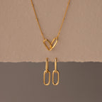 The Linked Charm Necklace and Earrings Set features two interlocking heart-shaped links and matching gold earrings, making an elegant anniversary gift displayed on a beige background.