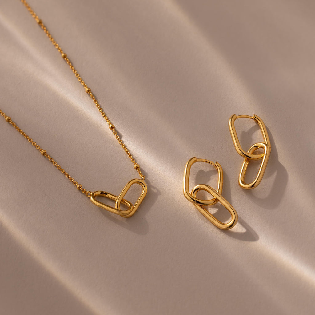 Linked Charm Necklace and Earrings Set in 18K Gold displayed on a beige surface with soft shadows—an elegant anniversary gift idea.