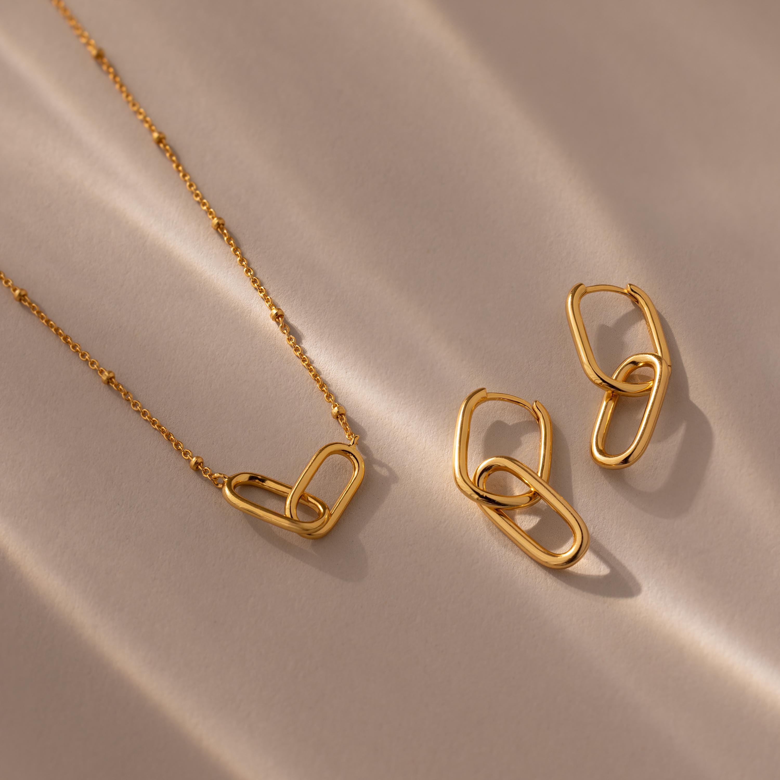 Linked Charm Necklace and Earrings Set in 18K Gold displayed on a beige surface with soft shadows—an elegant anniversary gift idea.