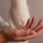 A hand holds the Fingerprint Birthstone Teardrop Necklace, a personalized gold pendant featuring a fingerprint and birthstone—perfect for capturing unique moments.